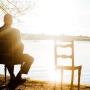 sitzender Mann alleine blickt auf den See, neben ihm ein leerer Stuhl