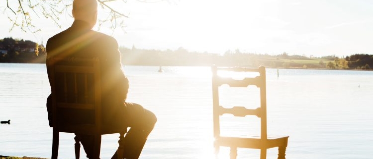sitzender Mann alleine blickt auf den See, neben ihm ein leerer Stuhl